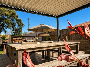 Um deck de madeira com uma mesa, um guarda-sol e uma garrafa de vinho.