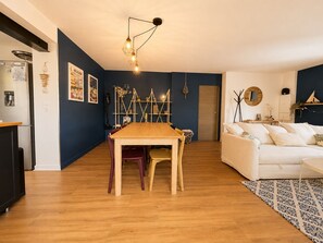 Ein zeitgemäßer Wohnraum mit einem Holzesstisch, einem weißen Sofa und einer Küchenzeile mit Kühlschrank.