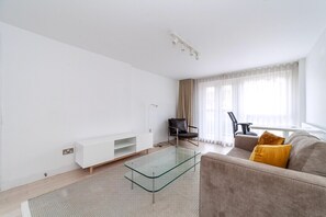 A modern living room with a glass coffee table, a sofa, a chair, and a TV stand. - Belgravia Living 2-bed Flat With Balcony (London)