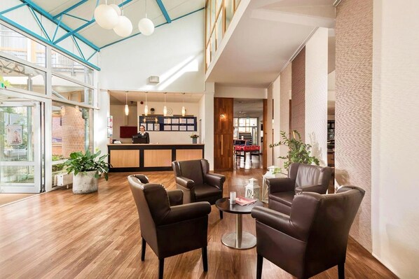 A hotel lobby with leather chairs, a reception desk, and a glass door entrance.