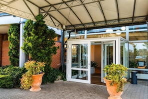 Una entrada techada con puerta de vidrio, plantas en macetas y fachada de edificio de ladrillo.