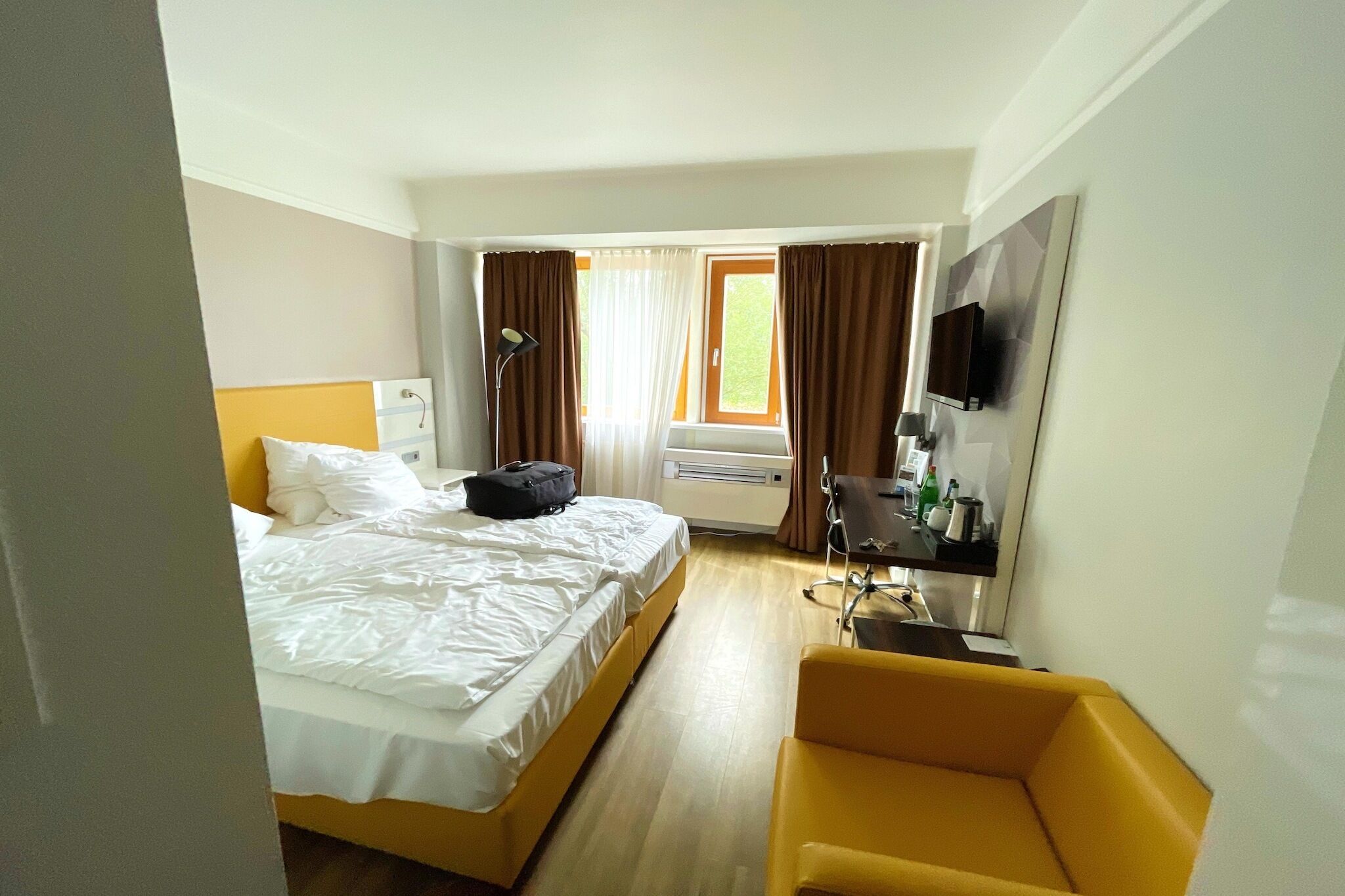 Une chambre d’hôtel avec un lit, un bureau, une chaise, une télévision et une fenêtre avec des rideaux.