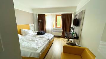 Une chambre d’hôtel avec un lit, un bureau, une chaise, une télévision et une fenêtre avec des rideaux.