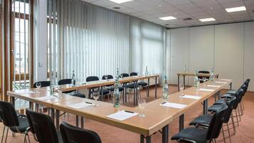 Una sala conferenze con lunghe tavolate, sedie e bottiglie d'acqua.