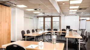 Ein Konferenzraum mit langen Tischen, Stühlen, einer Whiteboard-Tafel und einem Fenster mit Jalousien.