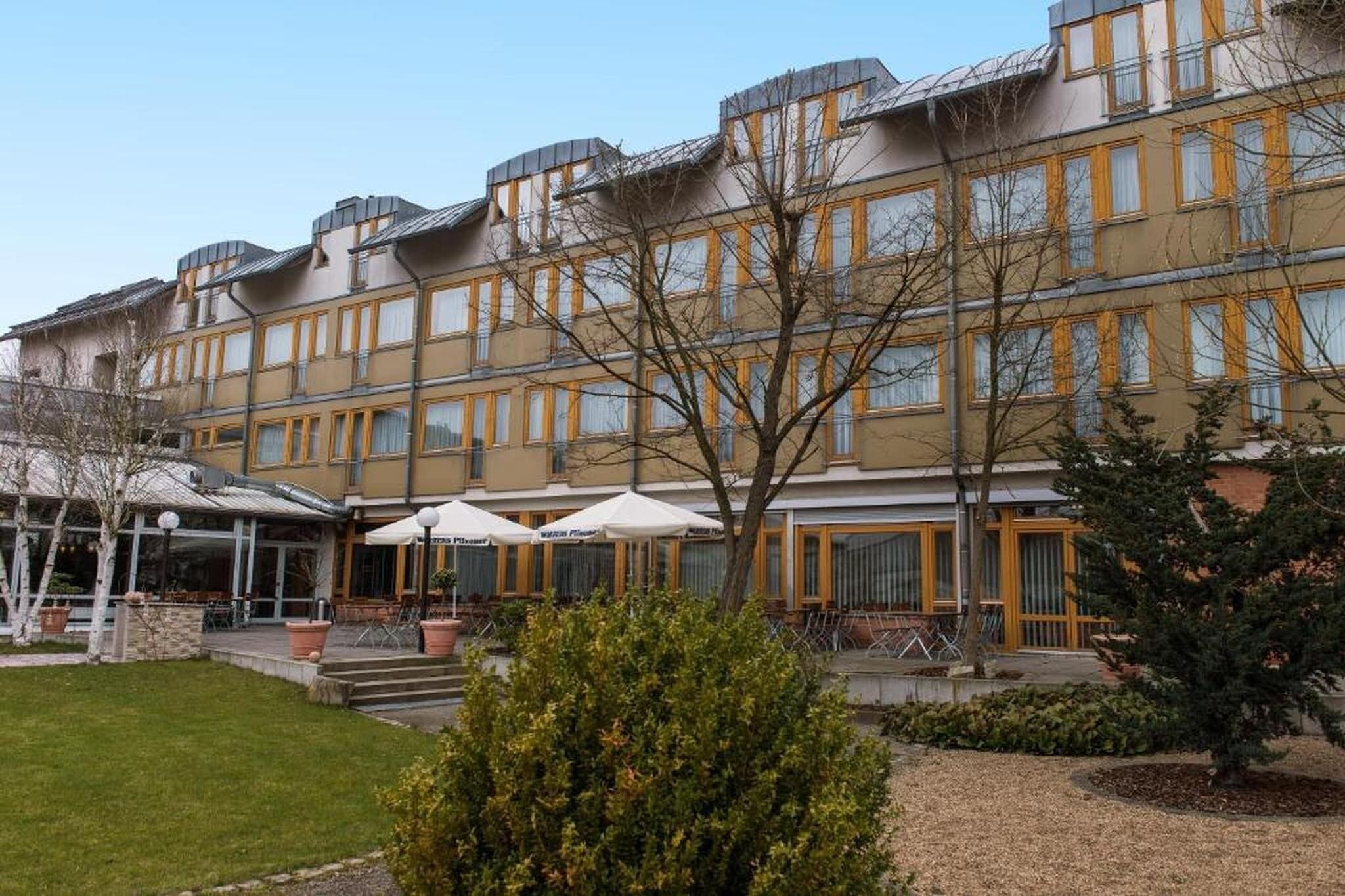 Ein mehrstöckiges Hotel mit einer Reihe von Balkonen, Außenplätzen und einem gepflegten Garten.