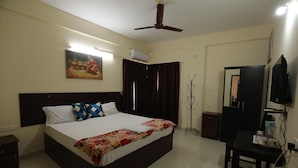 A bedroom with a bed, a ceiling fan, an air conditioner, a TV, a coat rack, and a small table. - Classique Inn | Near Padmanabhaswamy Temple (Thiruvananthapuram)