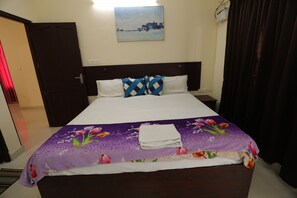 A neatly made bed with a floral bedspread, a cityscape painting on the wall, and a closed door. - Classique Inn | Near Padmanabhaswamy Temple (Thiruvananthapuram)