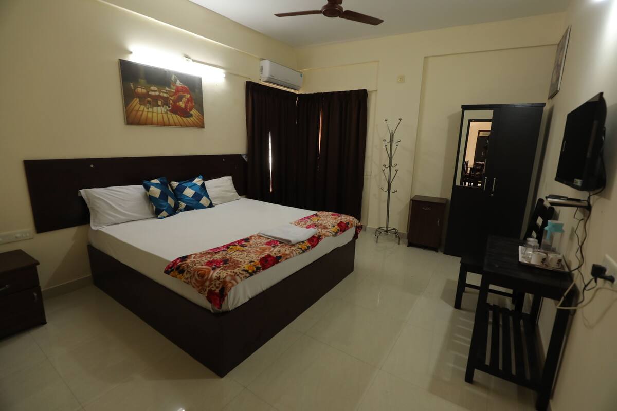 Habitación de hotel con cama, escritorio, silla, televisor y aire acondicionado.