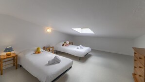 Een kamer met twee eenpersoonsbedden, een kleine tafel met een lamp, een dressoir en een dakraam.