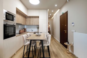 Une cuisine moderne avec des meubles blancs, un plan de travail en bois, une table à manger avec des chaises et une petite table ronde agrémentée d’un objet décoratif.