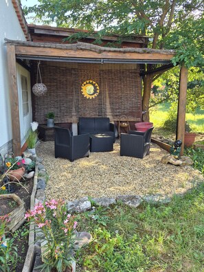 Ein überdachter Patio-Bereich mit Korbmöbeln, einer dekorativen Reifenwand und einem kleinen Garten mit Kieselsteinen und Pflanzen.