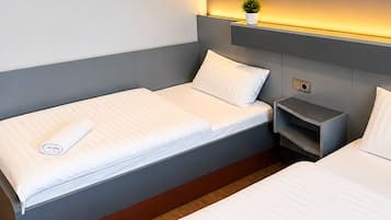 Una habitación de hotel moderna con dos camas, una mesita de noche y una pequeña planta en la pared.