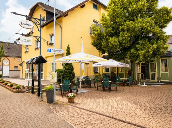 A yellow building with outdoor seating, a clock, and a sign for 'Hotel Panorama.' - Hotel Panorama (Nickenich)