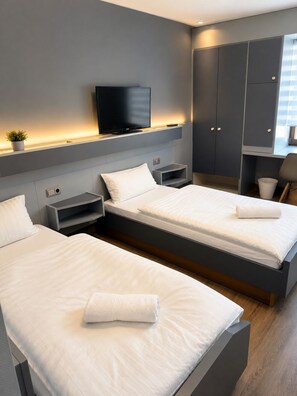 A modern hotel room with two beds, a TV, and a small plant.