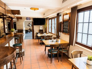 Interior de restaurante con mobiliario de madera, suelo de baldosas y un menú en la pizarra.