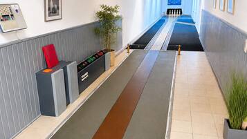 Een moderne hotelentree met een receptiebalie, een digitale informatiezuil en een lange gang die naar een zwembadgedeelte leidt.