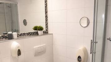 Un baño moderno con cabina de ducha de vidrio, un lavabo blanco, un inodoro y un espejo con detalles de mosaico.