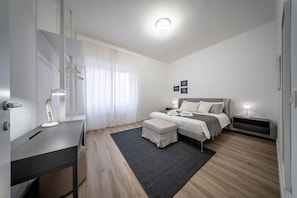 A modern bedroom with a bed, bedside tables, a desk, and a chair.