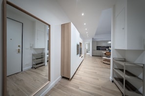 A modern interior with a hallway leading to a kitchen area, featuring light-colored flooring and minimalist decor.