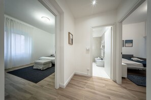 Ein modernes, helles Zimmer mit einem Bett, einer kleinen Sitzecke und einem durchgehenden Türrahmen einsehbaren Badezimmer.