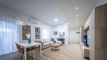 A modern living room with a dining area, a sofa, a TV, and a bookshelf.