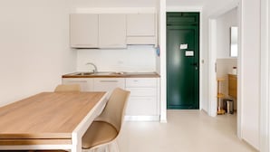 A modern kitchen with white cabinets, a wooden dining table, and a green door in the background. - Apartment with sea view terrace and air conditioning (Castelsardo)