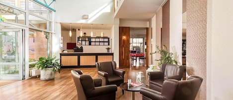 Eine Hotellobby mit Ledersesseln, einem Empfangstresen und einem Eingang mit Glastür.