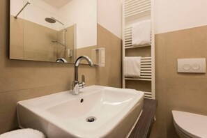 Ein modernes Badezimmer mit einem großen Waschbecken, einem Spiegel, einem Handtuchhalter und einer Toilette.