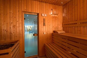 Ein Holz-Saunaraum mit Bänken, einer Glastür und einem Wandheizgerät.