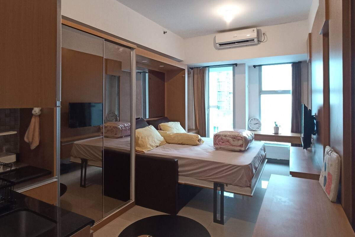 A modern hotel room with a bed, a round table, a mirror, and an air conditioning unit.
