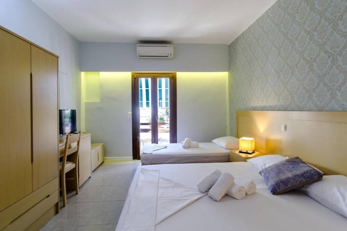 A hotel room with two beds, a desk with a television, a wardrobe, and a door leading outside.