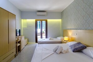 A hotel room with two beds, a desk with a television, a wardrobe, and a door leading outside.