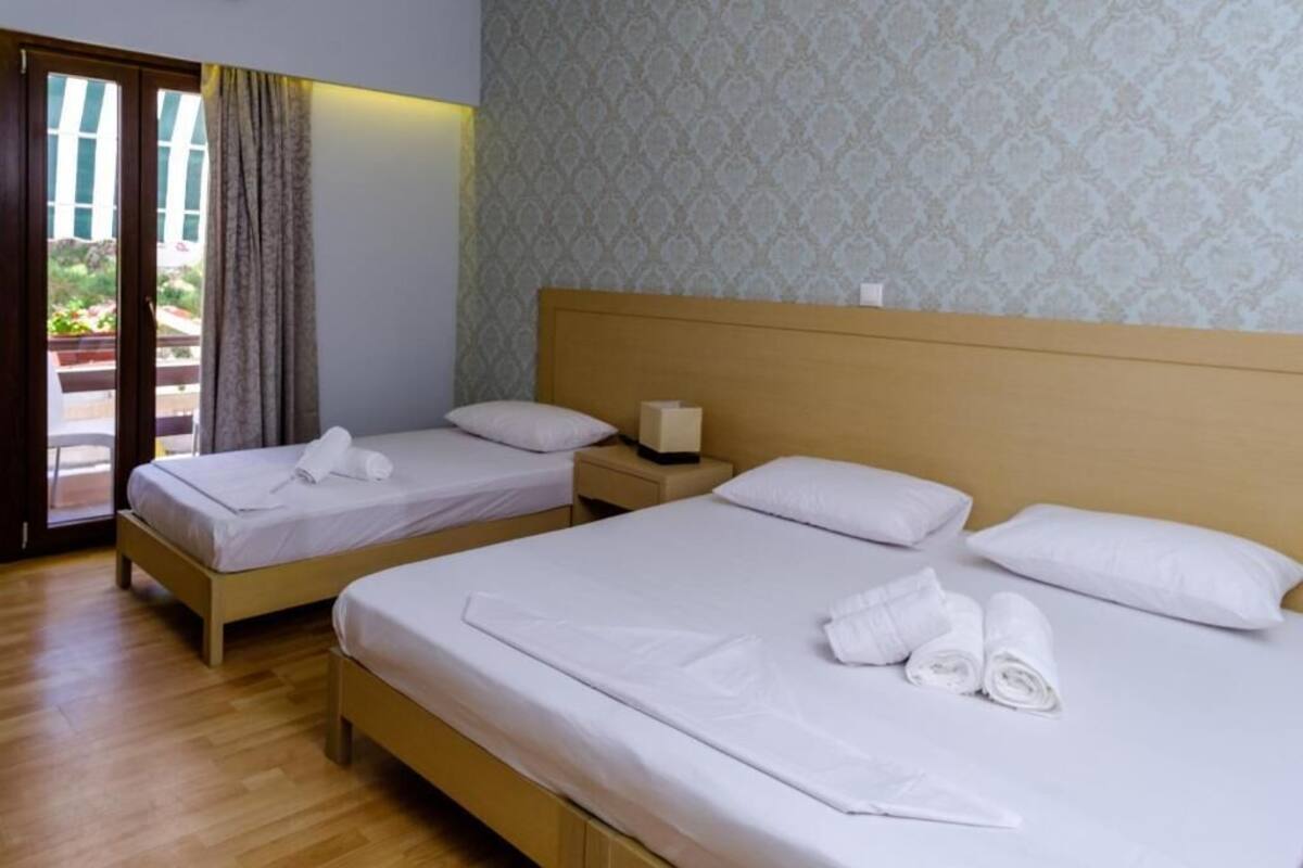 A hotel room with two beds, wooden headboards, a nightstand, and a patterned wallpaper.