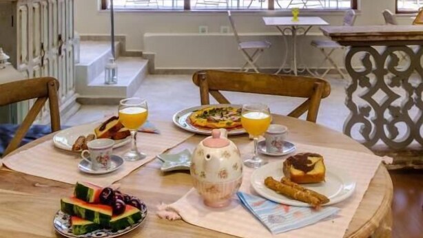 A dining area with a chandelier, a table set with breakfast, and a view of the outdoors. - Aphrodite Hotel Syros  (Syros)