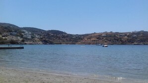 A coastal landscape with a calm sea, a sandy beach, and buildings on the hillside. - Aphrodite Hotel Syros  (Syros)