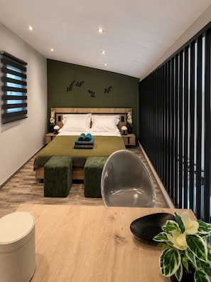 Une chambre moderne avec une tête de lit en bois, un lit avec une literie verte, deux tables de chevet avec des lampes, un banc recouvert d’un tissu vert, une chaise noire et une plante en pot.