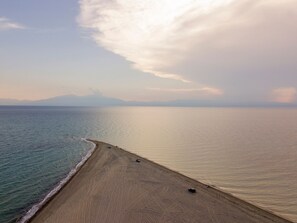 Een strand met heldere lucht, rustige zee en bergen in de verte.