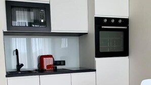 Una cocina compacta con muebles blancos, microondas, horno y un tostador rojo sobre la encimera.