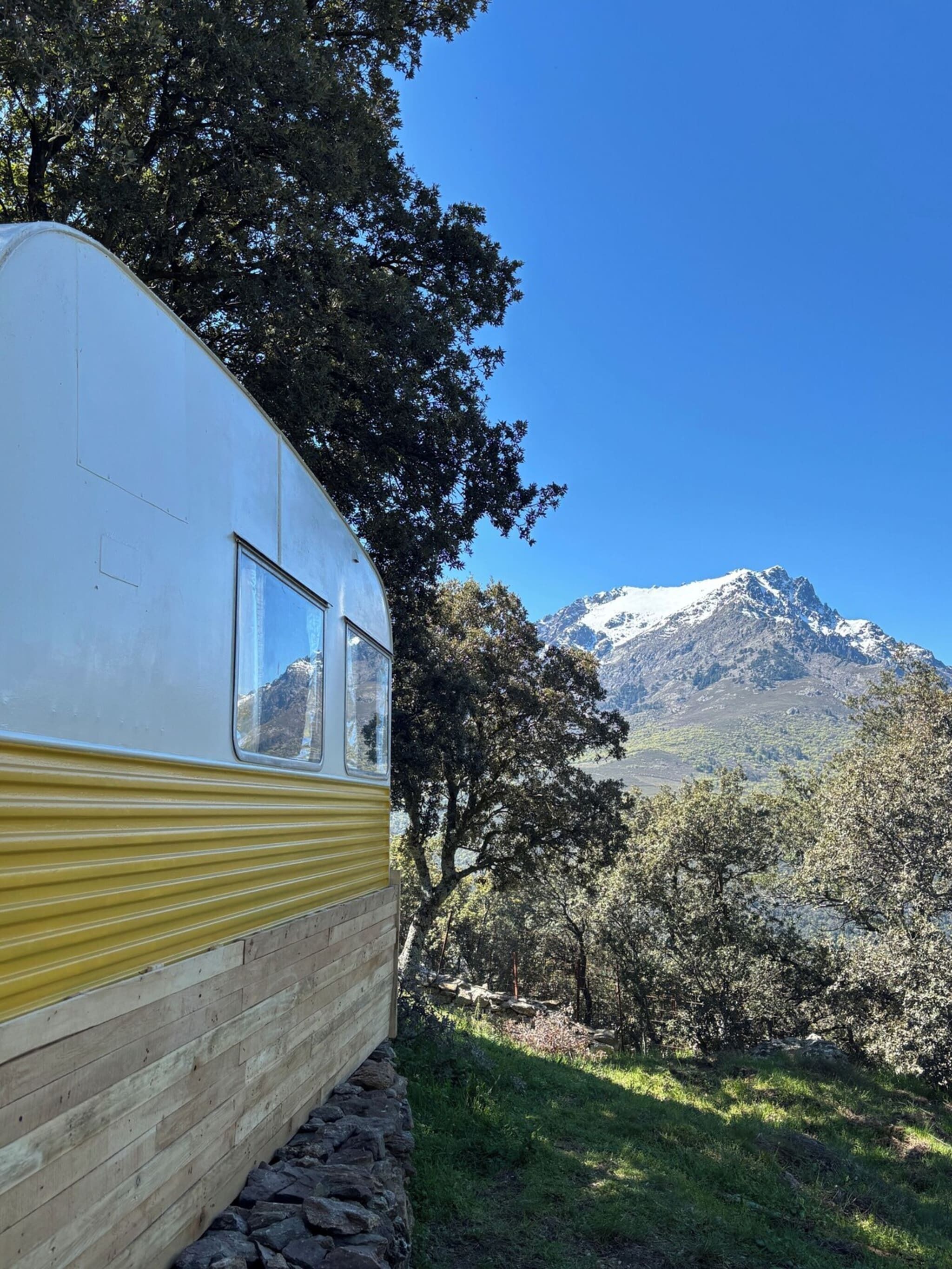 Een oldtimer camper met een raam, geparkeerd in een natuurlijke omgeving met een berg op de achtergrond.