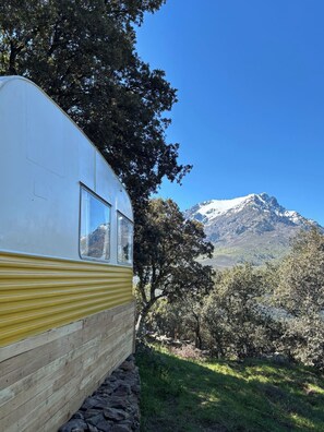 A vintage camper with a window, parked in a natural setting with a mountain in the background.