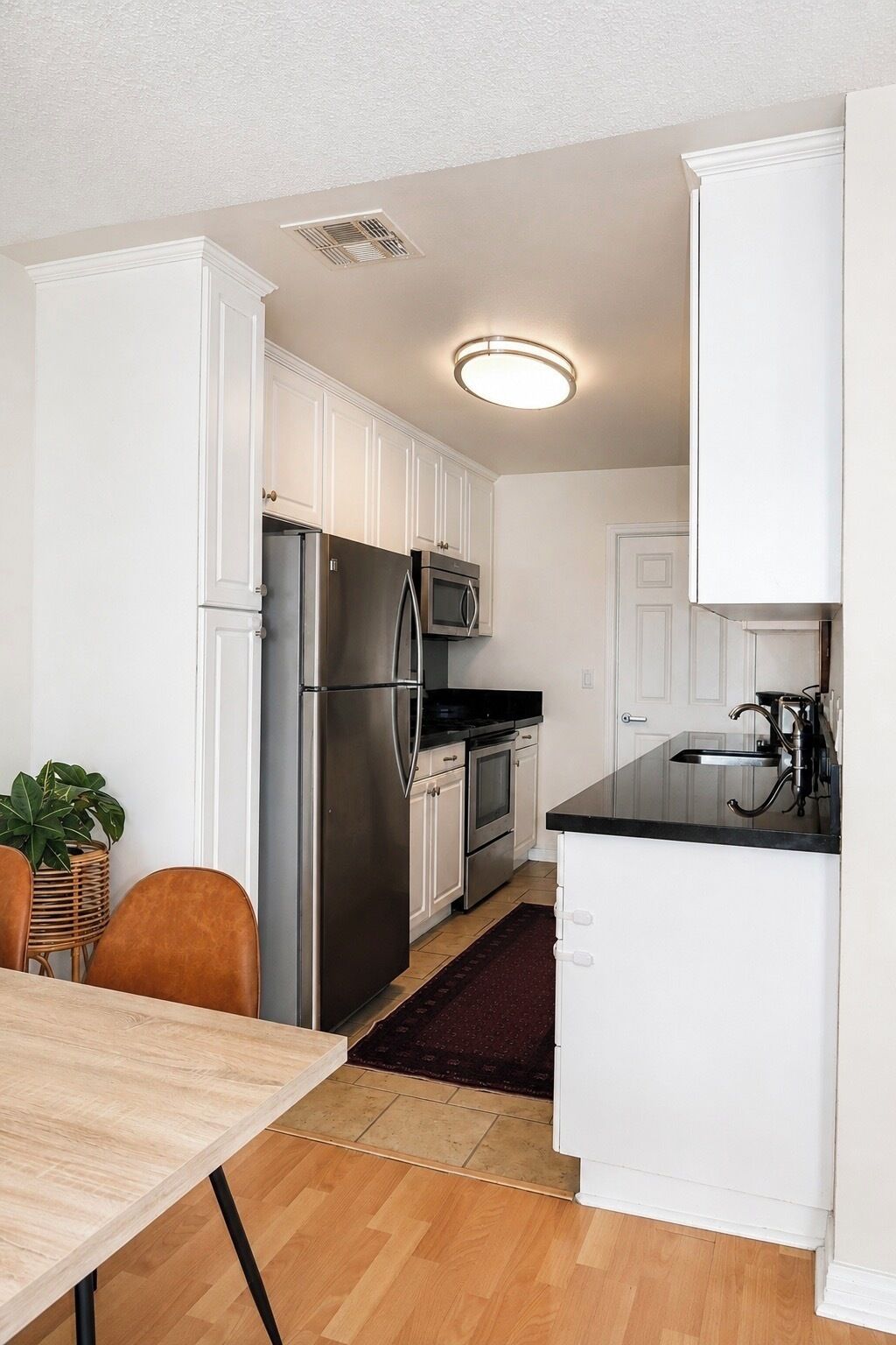 A compact kitchen with white cabinetry, a stainless steel refrigerator, a microwave, and a sink.