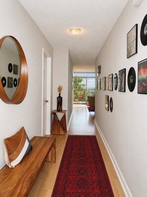 A hallway with a wooden bench, a red patterned rug, a mirror, and framed pictures on the walls. - BEST Ocean & Sunset views in Marina Del Rey - 12 mins from LAX & SoFi Stadium (Marina del Rey)