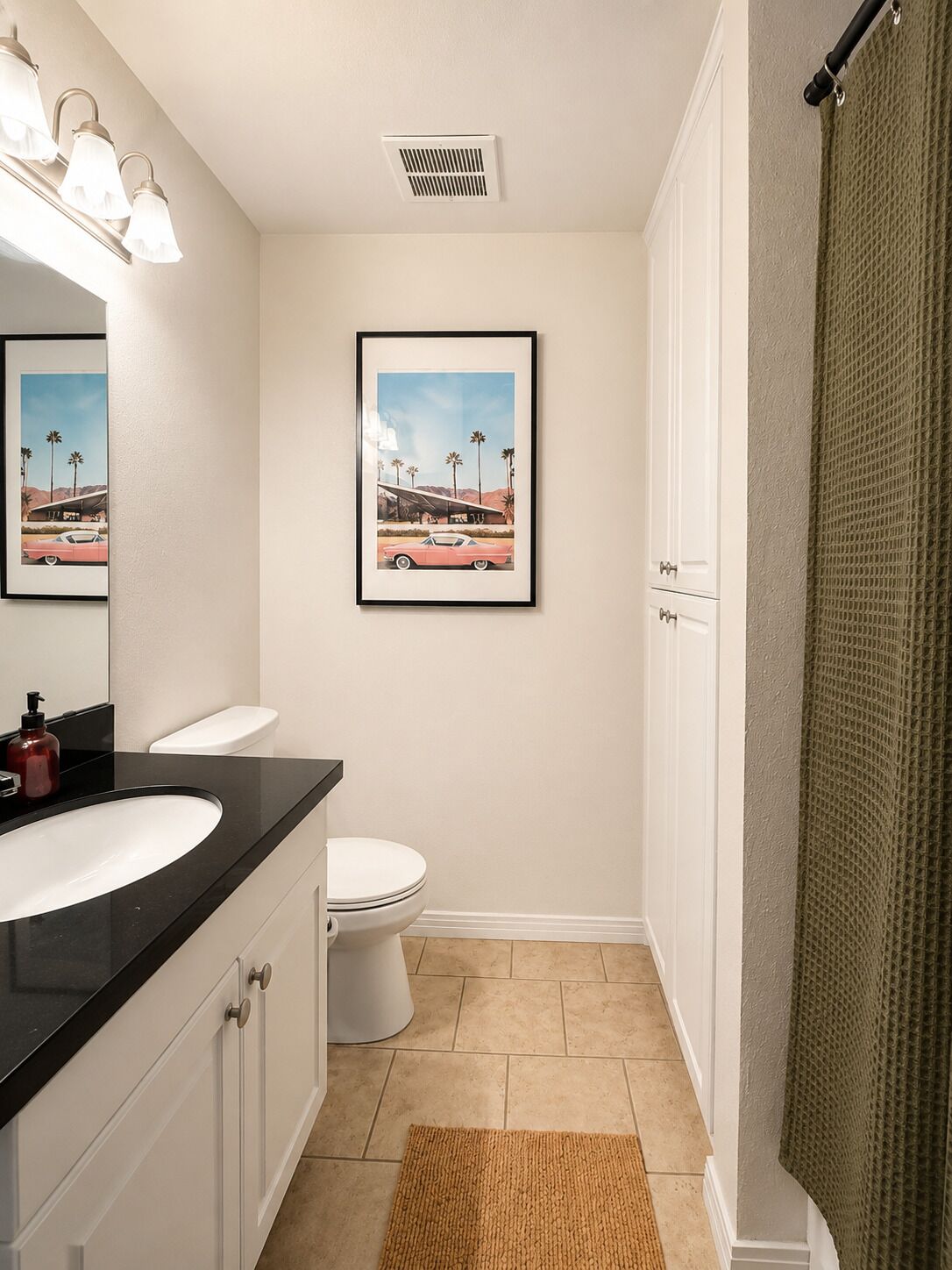 A bathroom with a white toilet, a black sink, a framed picture on the wall, and a shower curtain.