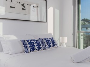 A hotel room with a bed, pillows, a lamp, and a window with a view. - Coastal Luxe Rooftop Escape - Paradiso 345 (Tweed)
