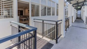 A covered outdoor corridor with a metal railing, a staircase, and a view into a room with a sofa and coffee table. - Coastal Luxe Rooftop Escape - Paradiso 345 (Tweed)