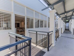 Ein überdachter Außenbereich mit Metallgeländer, einer Treppe und Blick in einen Raum mit Sofa und Couchtisch.