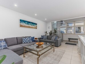 A modern living room with a grey sofa, a glass coffee table, and a painting of waves on the wall. - Coastal Luxe Rooftop Escape - Paradiso 345 (Tweed)