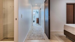 A hallway with a glass shower, a bed, and a dark wooden door. - Coastal Luxe Rooftop Escape - Paradiso 345 (Tweed)