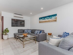 Ein modernes Wohnzimmer mit einem grauen Sofa, einem Glastisch und einem Gemälde einer Strandansicht an der Wand.
